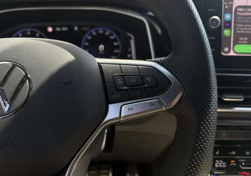 Gros plan sur le volant multifonction en cuir perforé du Volkswagen T-Roc 2025 avec commandes intégrées et tableau de bord digital en arrière-plan.