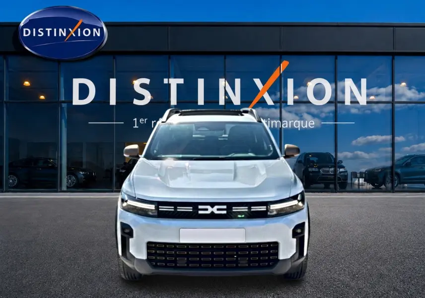 Vue frontale du Dacia Bigster blanc avec calandre noire et logo distinctif, devant une vitrine Distinxion.