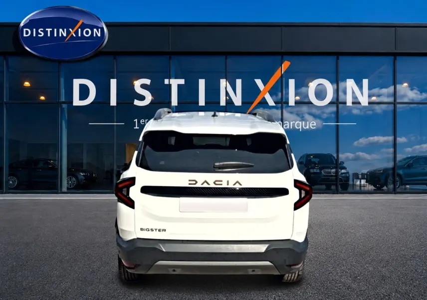 Vue arrière d'un Dacia Bigster blanc avec barres de toit et logo DACIA en relief sur fond de vitrine Distinxion.