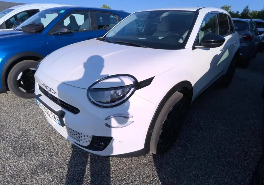 Vue 3/4 avant droit d'une FIAT 600 blanche 2025 avec phares ronds et détails noirs contrastants.