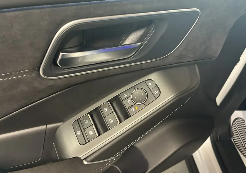 Gros plan sur la porte côté conducteur du Nissan Qashqai blanc nacré 2025, avec commandes électriques et poignée noire.