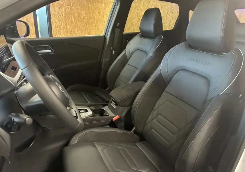 Vue intérieure côté conducteur du Nissan Qashqai 2025, sièges cuir noir avec logo Qashqai embossé et console centrale visible.