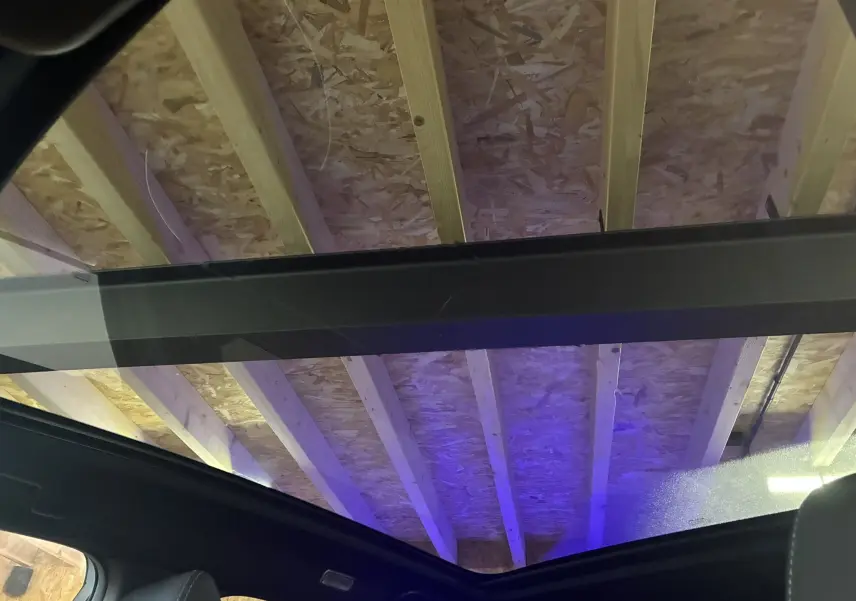 Vue intérieure du toit panoramique noir du Nissan Qashqai blanc nacré, soulignant la structure en bois du plafond au-dessus.