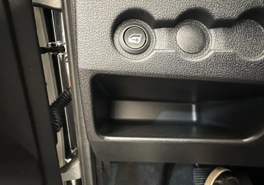 Détail du bouton d'ouverture du coffre côté conducteur dans l'habitacle noir de l'AIXAM AMBITION E CITY PACK 2025.