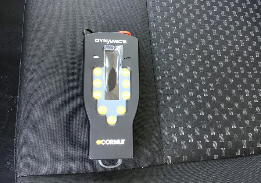 Télécommande noire du bras de levage Cornut posée sur un siège en tissu gris foncé à motifs.