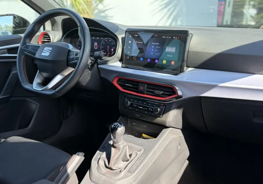 Vue intérieure côté conducteur du tableau de bord et console centrale d'une SEAT IBIZA TSI 115 FR avec détails rouges et écran tactile.