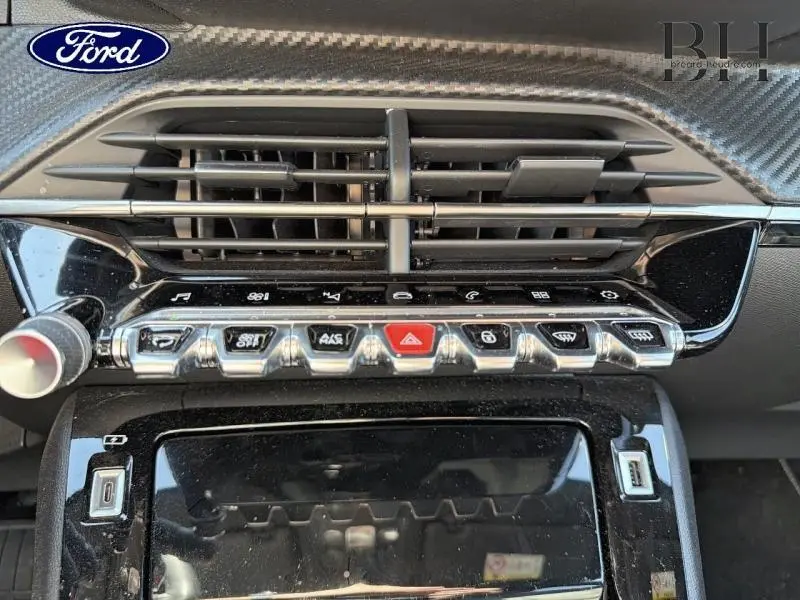 Vue rapprochée de la console centrale noire brillante du Peugeot 2008 blanc nacré, avec boutons chromés et aérateurs horizontaux.