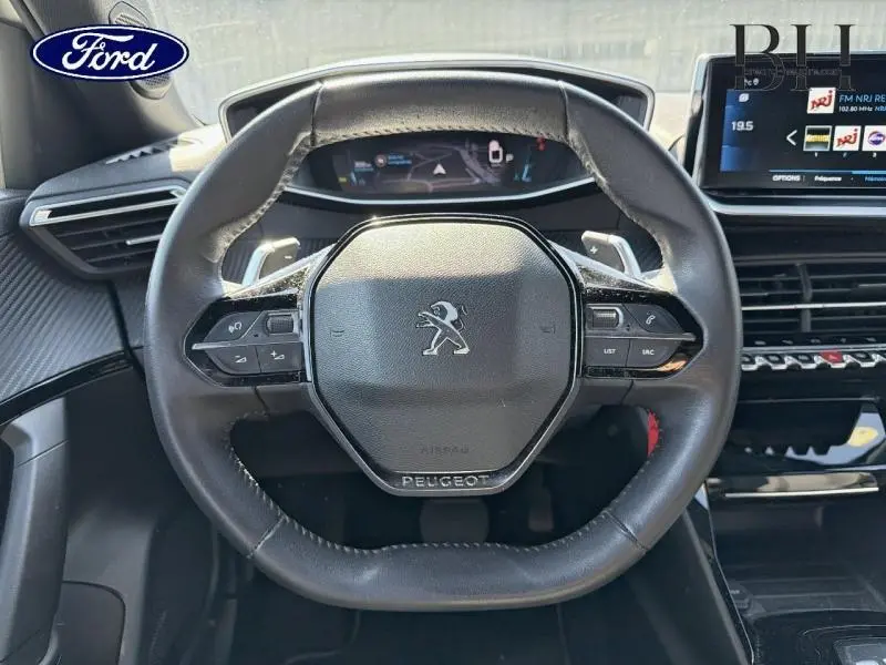 Vue rapprochée du volant cuir noir de la Peugeot 2008 avec commandes intégrées et tableau de bord numérique.