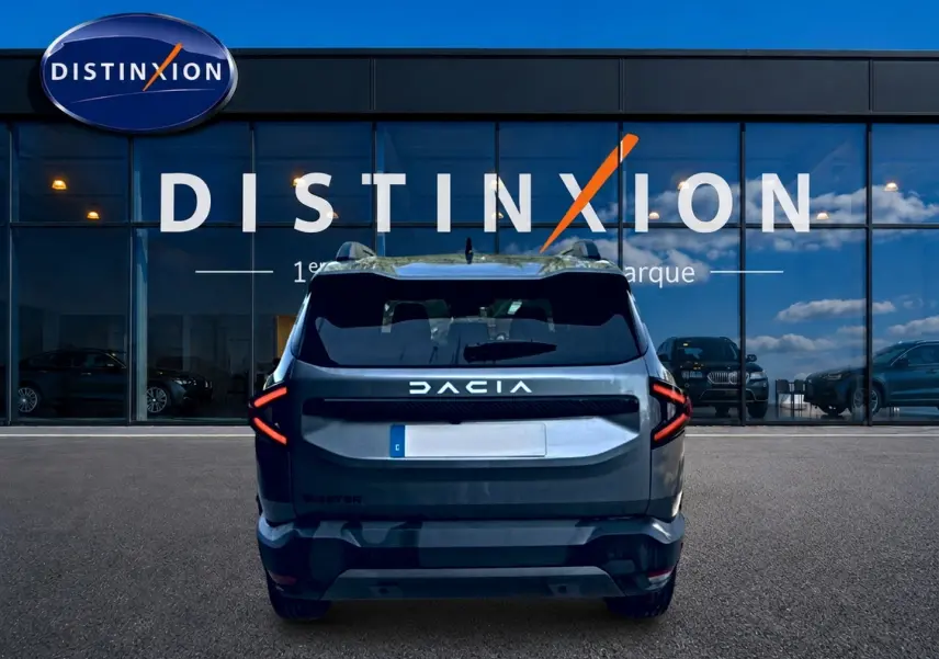 Vue arrière d'un Dacia Bigster gris schiste, avec feux arrière LED en forme de flèche, devant une vitrine Distinxion.