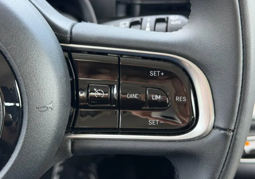 Gros plan sur les commandes du régulateur de vitesse au volant noir de la Fiat 500 électrique blanche 2023.