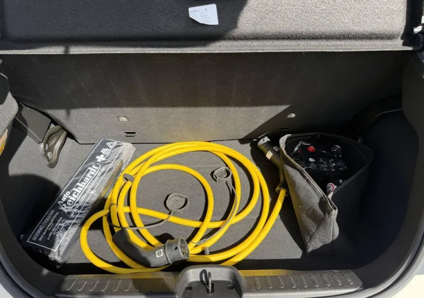 Coffre ouvert de la Fiat 500 électrique blanche MY23 montrant un câble de recharge jaune et un kit de secours.