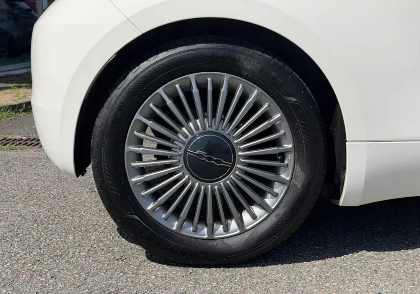 Gros plan sur la roue arrière droite blanche d'une Fiat 500 e 118ch MY23 avec jante argentée à rayons fins.