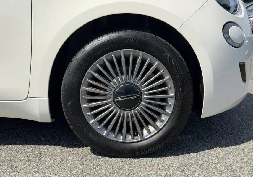 Gros plan sur la roue avant droite d'une Fiat 500 électrique blanche, avec jante argentée au design rayonné.