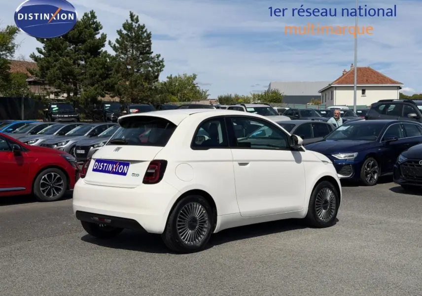 Vue 3/4 arrière droite d'une Fiat 500 électrique blanche 2023 avec jantes spécifiques et becquet arrière.