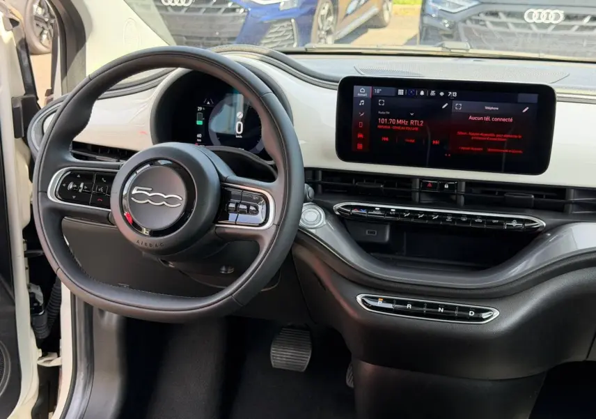 Vue intérieure du poste de conduite de la Fiat 500 e blanche 2023, avec volant multifonction et écran tactile central.