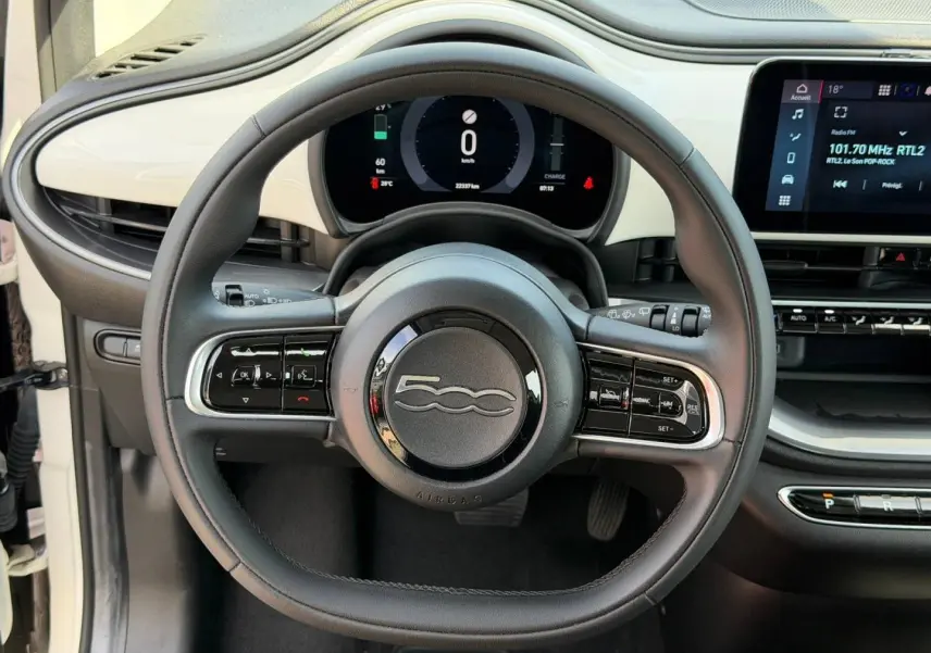 Vue rapprochée du volant noir de la Fiat 500 électrique blanche MY23 avec tableau de bord numérique et écran tactile.