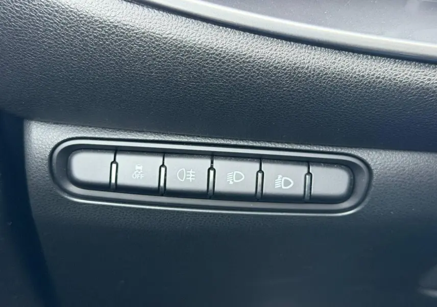 Gros plan sur les boutons de commande d'éclairage et d'assistance sur la planche de bord noire d'une Fiat 500 électrique blanche.