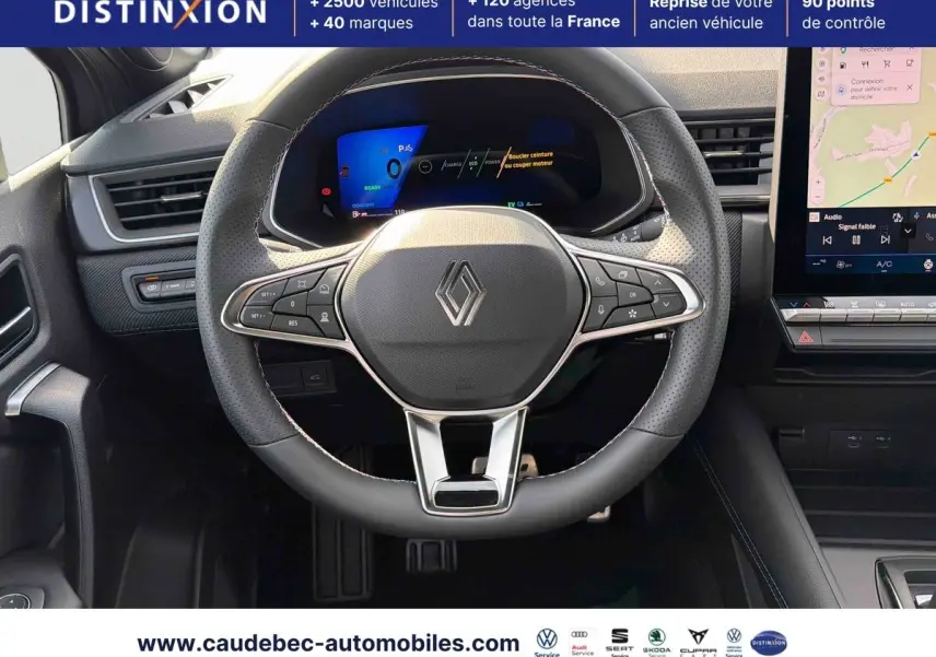 Vue rapprochée du volant noir perforé avec logo Renault et tableau de bord numérique lumineux du Symbioz E-Tech.