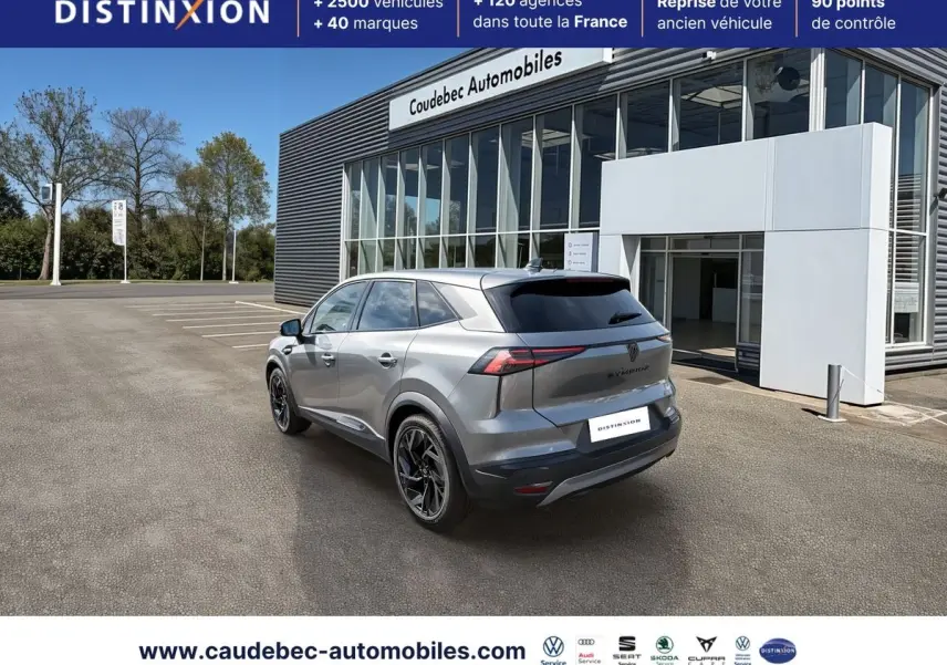 Vue 3/4 arrière droite d'un Renault Symbioz gris métallisé avec jantes noires devant un bâtiment moderne.
