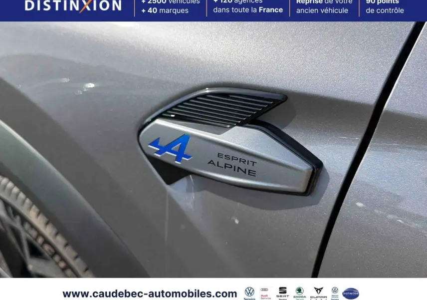 Gros plan sur l'emblème Esprit Alpine bleu et noir sur la carrosserie grise métallisée côté avant droit du Renault Symbioz.