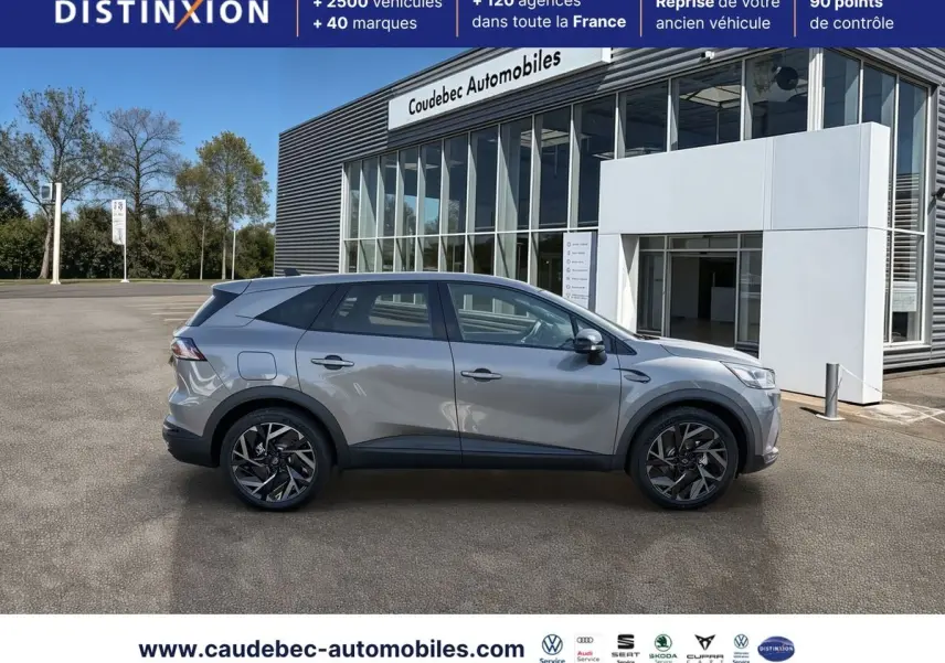 Vue de profil côté gauche d’un Renault Symbioz gris métallisé, avec jantes alliage 19 pouces, devant un bâtiment commercial.