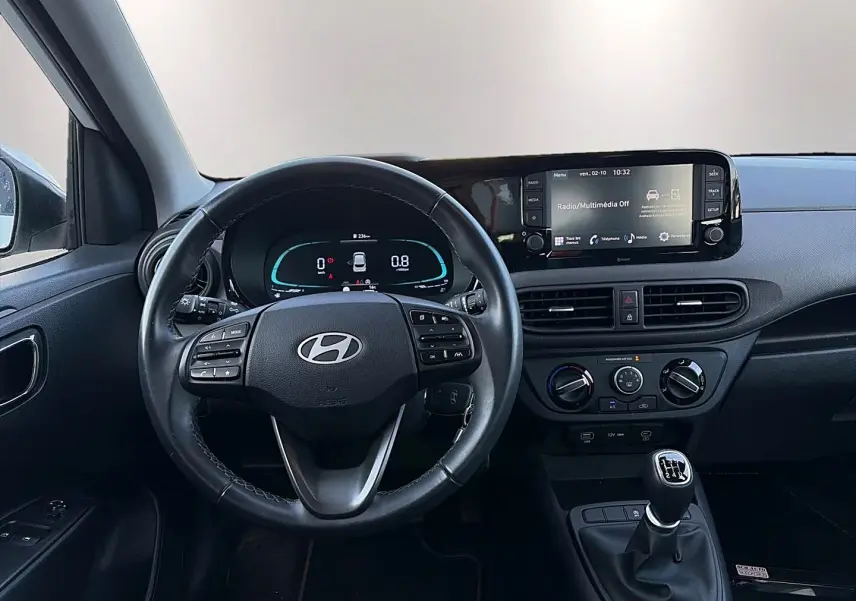 Vue intérieure du tableau de bord et volant cuir multifonction d'une Hyundai i10 blanche avec boîte manuelle et écran tactile.