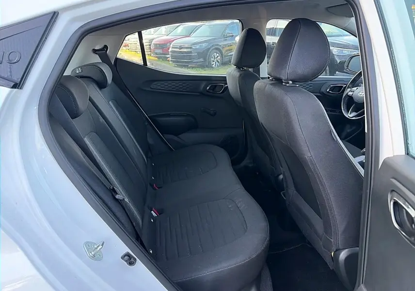Vue intérieure côté gauche montrant la banquette arrière noire et les sièges avant d'une Hyundai i10 blanche 2024.