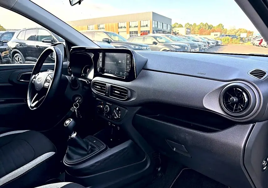 Intérieur avant droit de la Hyundai i10 blanche 2024, volant cuir, écran tactile et levier de vitesses manuel visible.