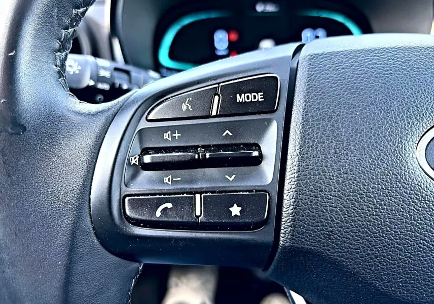 Gros plan sur les commandes audio et téléphoniques au volant cuir noir de la Hyundai i10 blanche 2024.
