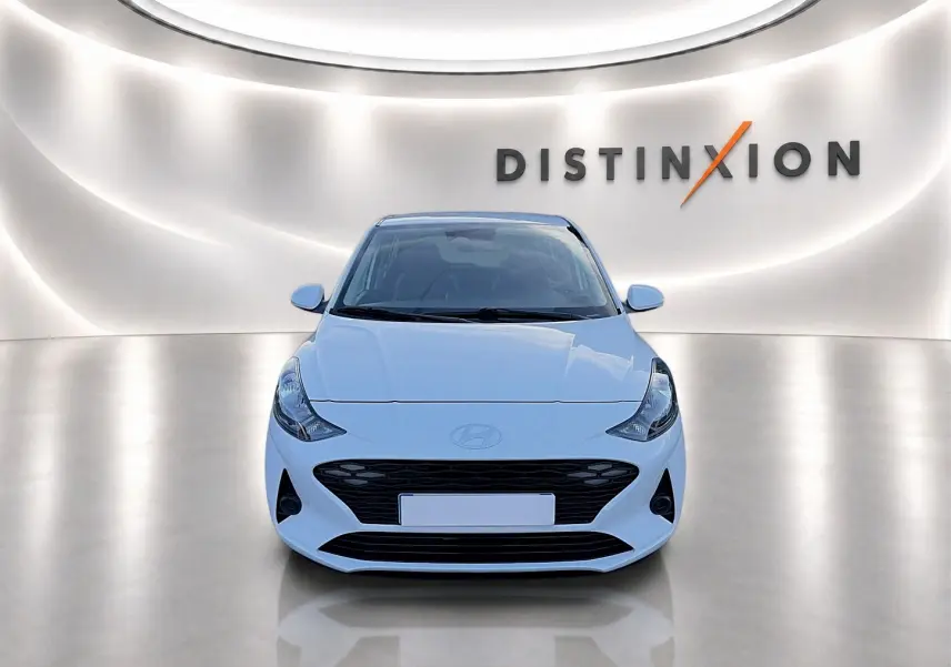 Vue avant d'une Hyundai i10 blanche 2024 dans un showroom lumineux avec logo Distinxion en arrière-plan.