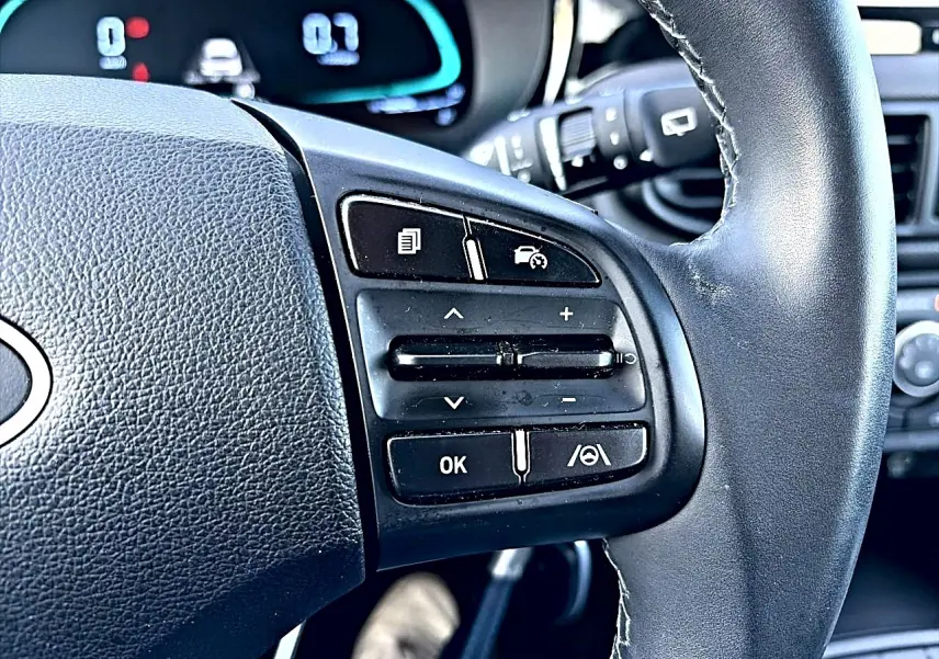 Gros plan sur les commandes multifonctions à droite du volant cuir noir d'une Hyundai i10 blanche de 2024.
