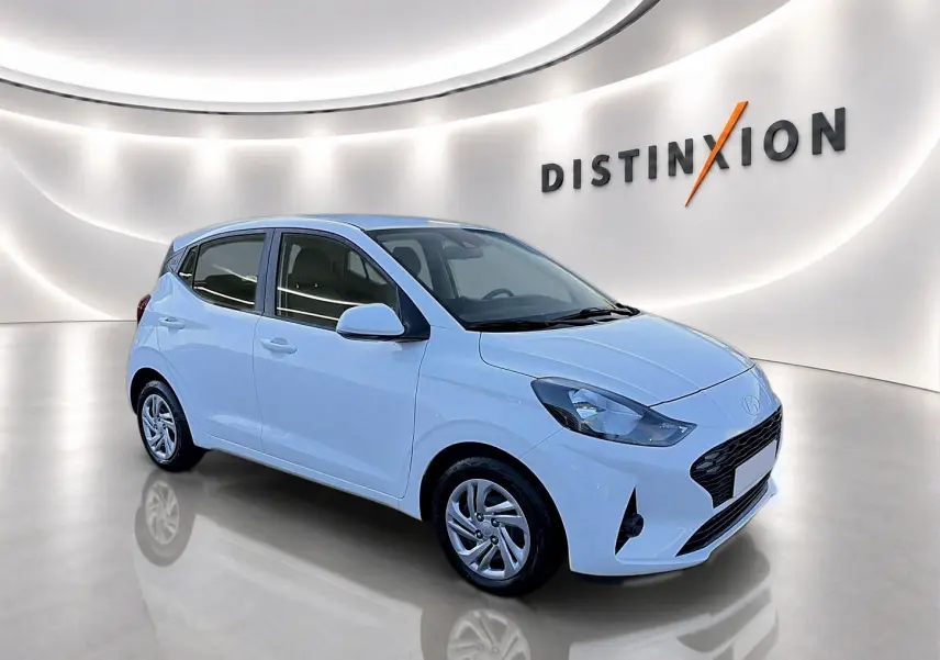 Hyundai i10 blanc vue 3/4 avant droit dans un showroom lumineux avec logo Distinxion en arrière-plan.