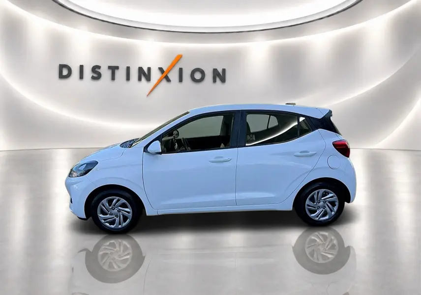 Profil droit de la Hyundai i10 blanche 2024, compacte et moderne, sur fond lumineux avec logo Distinxion en arrière-plan.