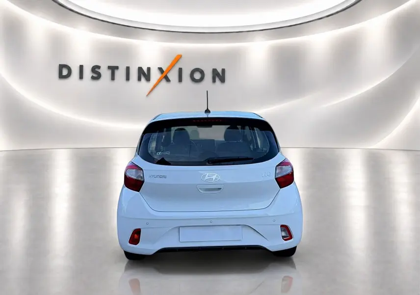 Vue arrière d'une Hyundai i10 blanche 2024 dans un showroom lumineux avec logo Distinxion en arrière-plan.