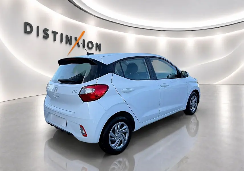 Vue 3/4 arrière droite d'une Hyundai i10 blanche 2024 dans un showroom lumineux avec logo Distinxion en arrière-plan.