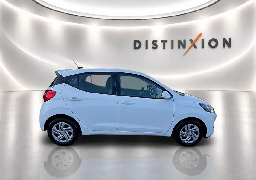 Profil droit d'une Hyundai i10 blanche 2024 dans un studio lumineux avec logo Distinxion en arrière-plan.