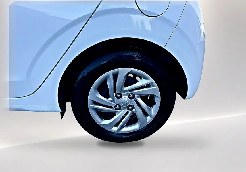 Gros plan sur la roue arrière droite d'une Hyundai i10 blanche avec jante alliage et passage de roue arrondi.