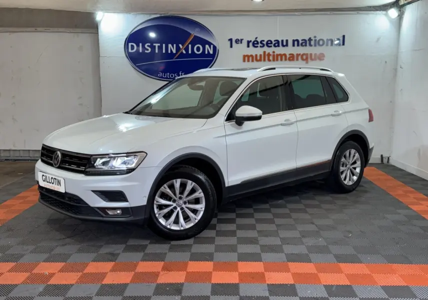 Volkswagen Tiguan blanc vu de 3/4 avant droit dans un showroom avec jantes alliage et barres de toit noires.