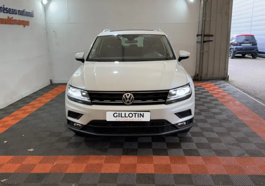Volkswagen Tiguan blanc vue de face dans un showroom avec phares LED allumés et calandre noire.