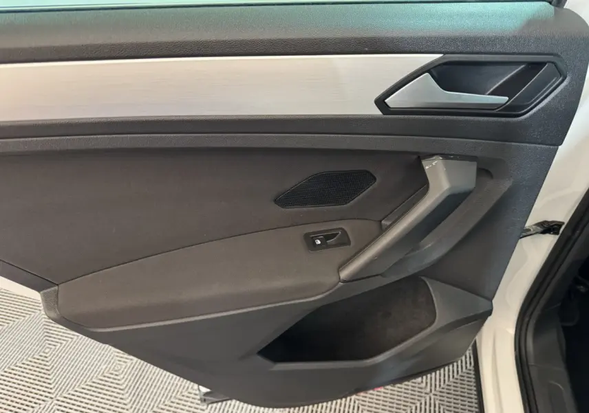 Intérieur côté gauche de la porte avant blanche du Volkswagen Tiguan 2020, avec garniture noire et poignée grise.