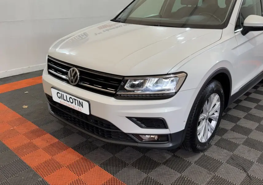 Vue 3/4 avant droit d'un Volkswagen Tiguan blanc avec phares LED allumés et jantes alliage.