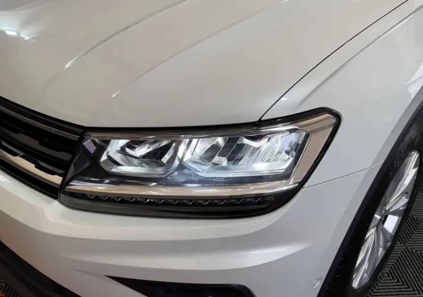 Gros plan sur le phare avant droit et la calandre du Volkswagen Tiguan blanc 2020, finition Confortline.