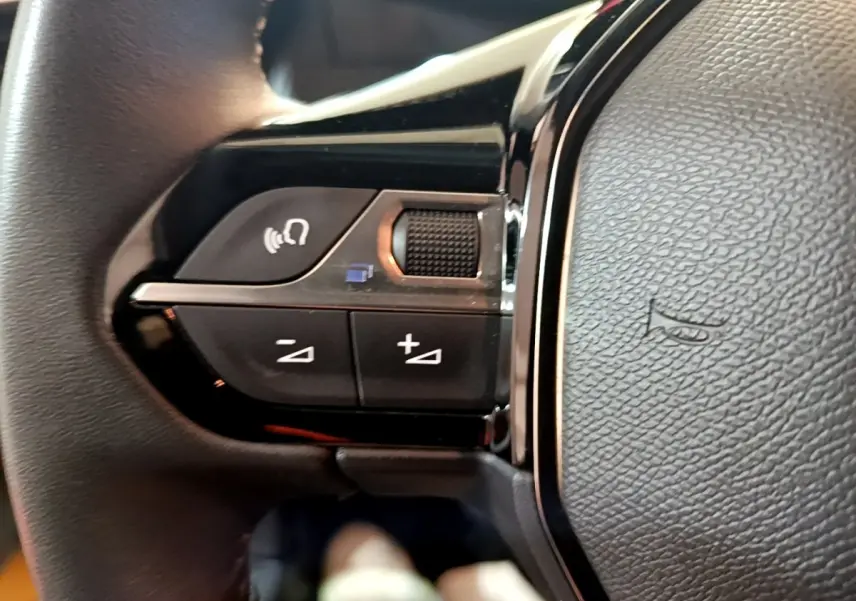 Gros plan sur les commandes multifonctions gauche du volant cuir de la Peugeot 208 jaune 2023.