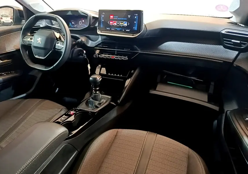Intérieur avant de la Peugeot 208 PureTech 100 S&S Allure Pack 2023, vue côté conducteur avec tableau de bord numérique et volant cuir.