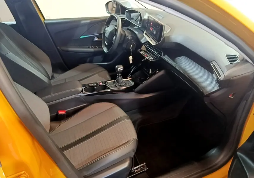 Vue intérieure côté conducteur d'une Peugeot 208 jaune 2023, volant cuir multifonctions et écran tactile central visible.