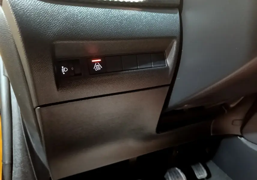 Détail du tableau de bord côté gauche de la Peugeot 208 jaune, avec commandes d'éclairage et assistance désactivée.