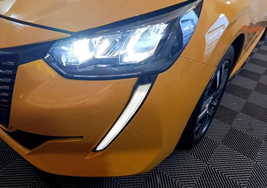 Gros plan sur l'avant droit jaune vif de la Peugeot 208 2023 avec phares LED allumés et jante noire.