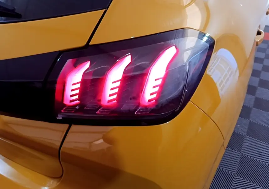 Gros plan sur le feu arrière droit allumé d'une Peugeot 208 jaune PureTech 100 S&S Allure Pack 2023.