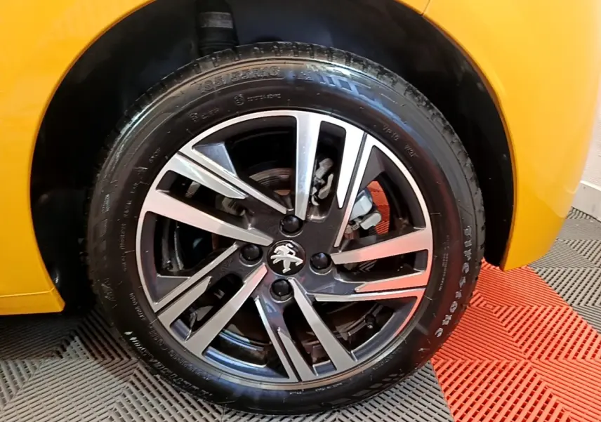 Gros plan sur la roue avant droite d'une Peugeot 208 jaune 2023 avec jante alliage noire et argentée.