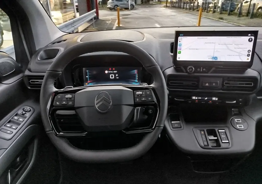 Vue intérieure centrée sur le volant et le tableau de bord numérique du Citroën Berlingo gris acier avec écran tactile de navigation.